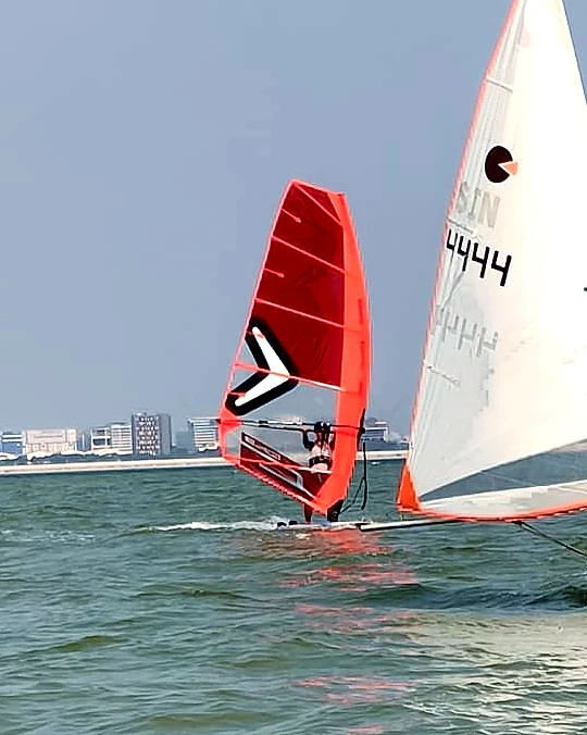 A red windsurfing sail alongside a SeaQuest dinghy